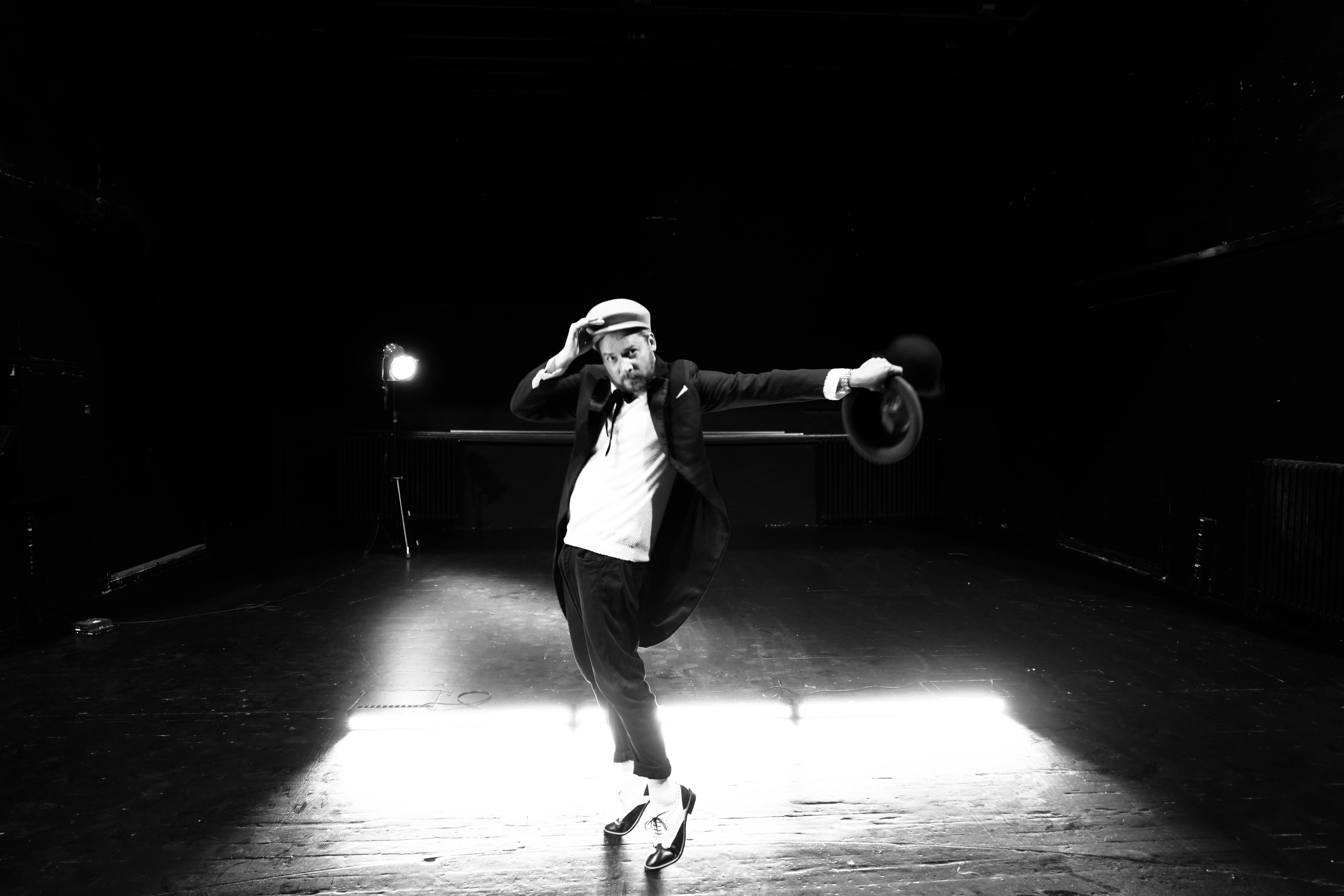 Taavi Teplenkov, Eesti Draamateatri näitleja. Mustvalge foto mehest, kes on üksi laval ja tantsupoosis. Ta on tõusnud varvastele, parema käega hoiab kinni heleda mütsi äärest, vasak käsi musta kaabuga on kõrvale sirutatud. Tal on seljas must frakk, jalas veidi üleskääritud äärtega mustad püksid ning musta ja valgega kingad. Tagaplaanil üks jalgadel põlev teatriprožektor ja mehe taga põrandal kolm eredalt põlevat valgusriba.