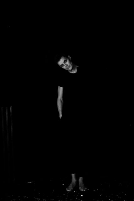 Tõnis Niinemets, Eesti Draamateatri näitleja. Mustvalge foto paljajalu noormehest, kes seisab tumedal taustal, kehahoiak veidi kallutatud ja pea viltu. Ta kannab musta riietust, mis sulandub taustaga, jättes esile vaid näo, käsivarre ja jalalabad. Tema pilk on intensiivne ja mõtlik.