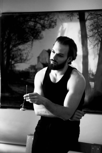 Märten Metsaviir, Eesti Draamateatri näitleja. Mustvalge foto noorest mehest, kellel on seljas must maika ja jalas tumedad püksid. Tal on tume habe ja tumedad vuntsid, silmi rõhutab tumedam meik. Nägu on tõsine. Mees hoiab käes ühte lühikese varrega lilleõit. Mees toetub istudes mööblidetailile, selja taga on suurendatud mustvalge ajalooline foto Draamateatri majast.