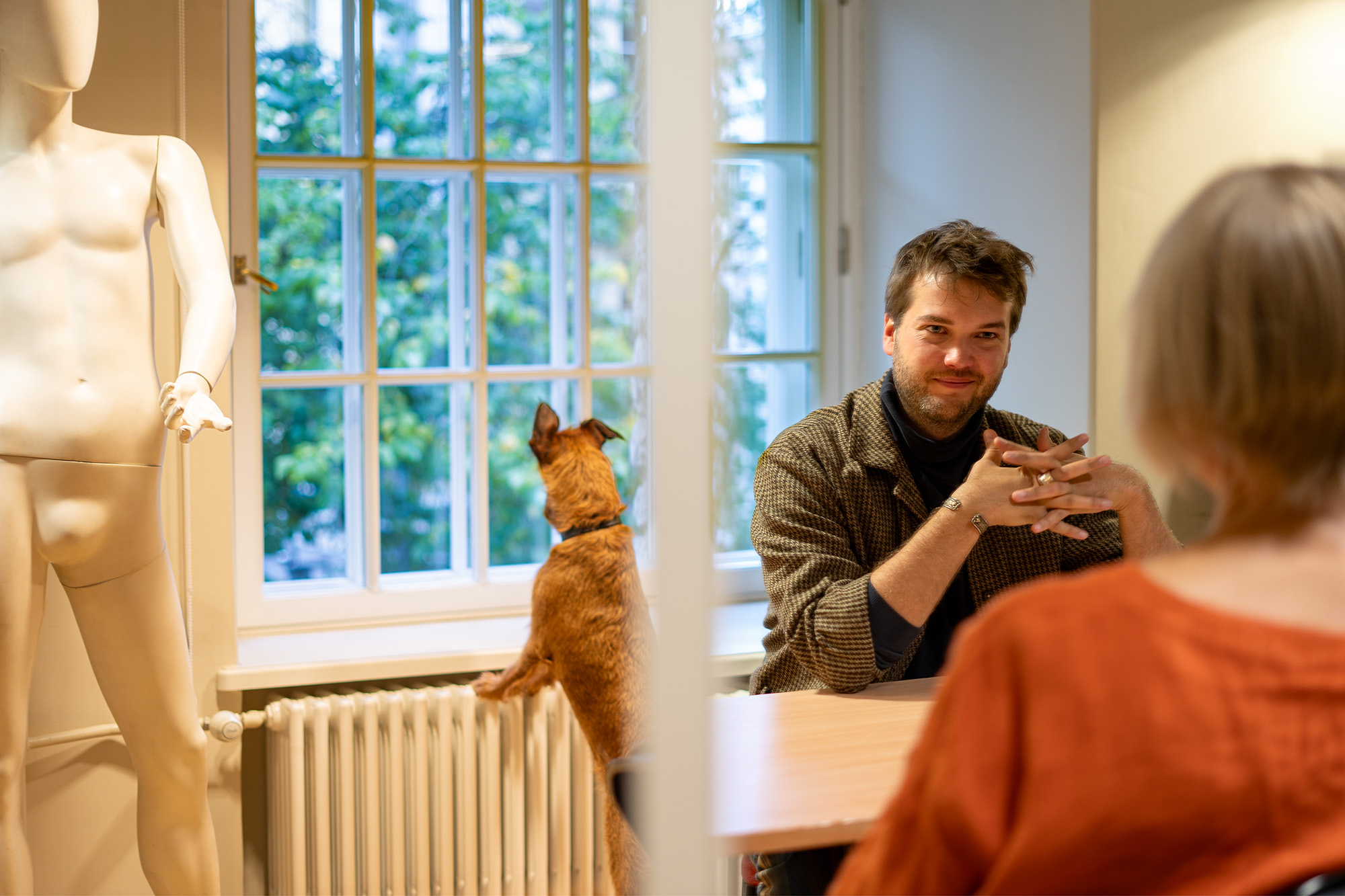 Lavastaja Johan Elm istub laua taga ja annab intervjuud, selja taga on ruutudega aken, koer toetub aknaalusele radiaatorile ja vaatab aknast välja